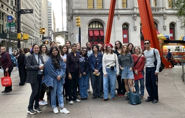 Large group of people smiling for a picture in front of red modern sculpture in downtown area