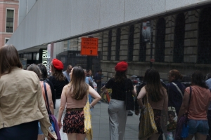 Group of people led by a tour guide walking down a street reflected on marble surface of a building