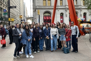 Large group of people smiling for a picture in front of red modern sculpture in downtown area